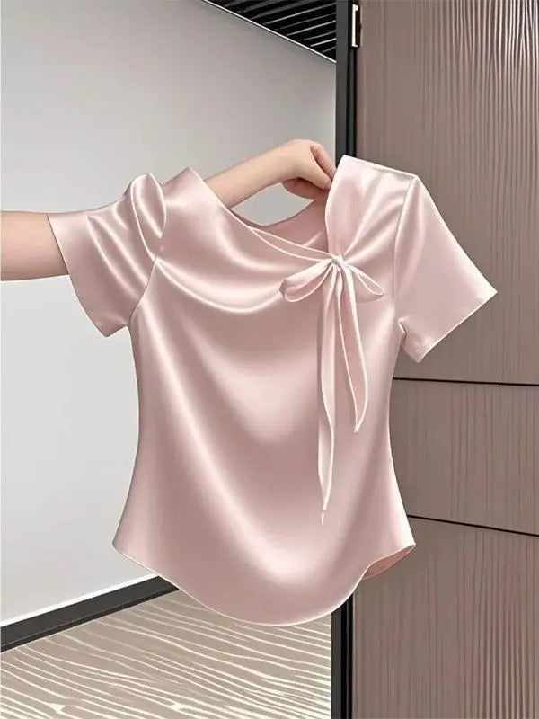 Pink satin blouse with a bow detail held by a hand against a neutral background